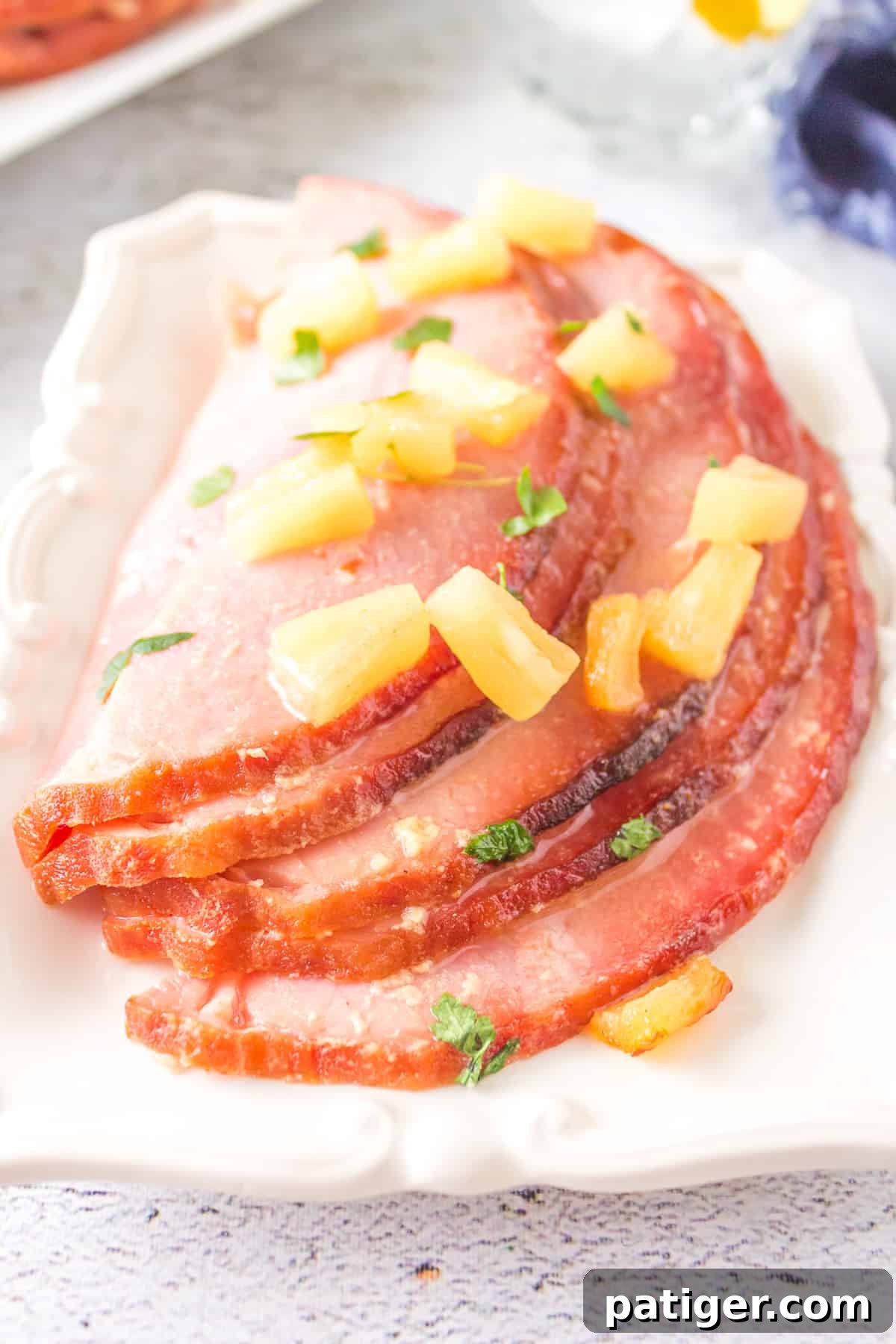 Perfectly carved slices of glazed ham adorned with glistening pineapple chunks, arranged neatly on a pristine white platter, showcasing its mouth-watering texture.