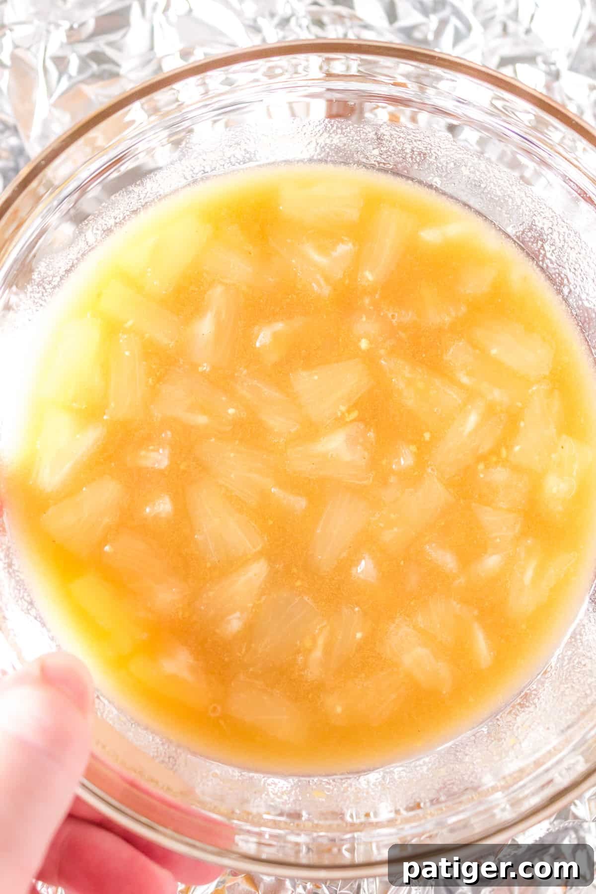 A small glass bowl filled with the vibrant maple pineapple glaze, showcasing the golden liquid with visible pineapple chunks, ready to be drizzled over the ham.