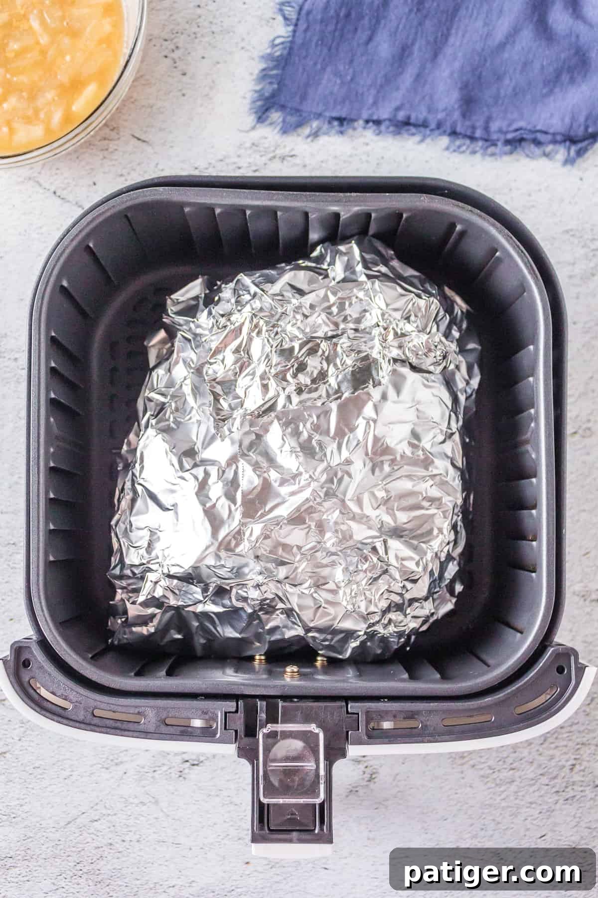 Foil-wrapped spiral ham resting inside an air fryer basket, positioned centrally for even cooking.