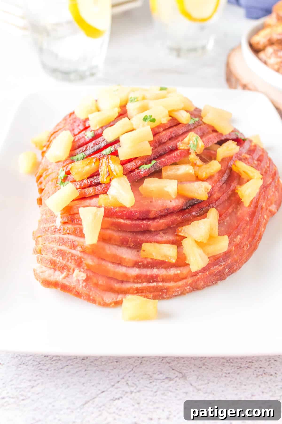 A magnificent pineapple glazed air fryer ham, crowned with fresh pineapple pieces, beautifully presented on a large white platter, ready for carving.