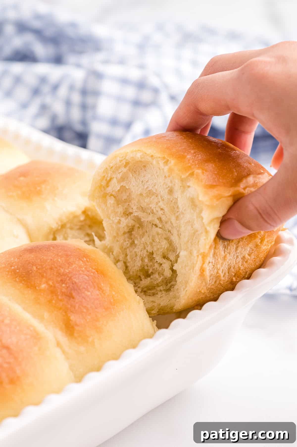 Hand pulling freshly baked potato roll out of corner of white baking dish