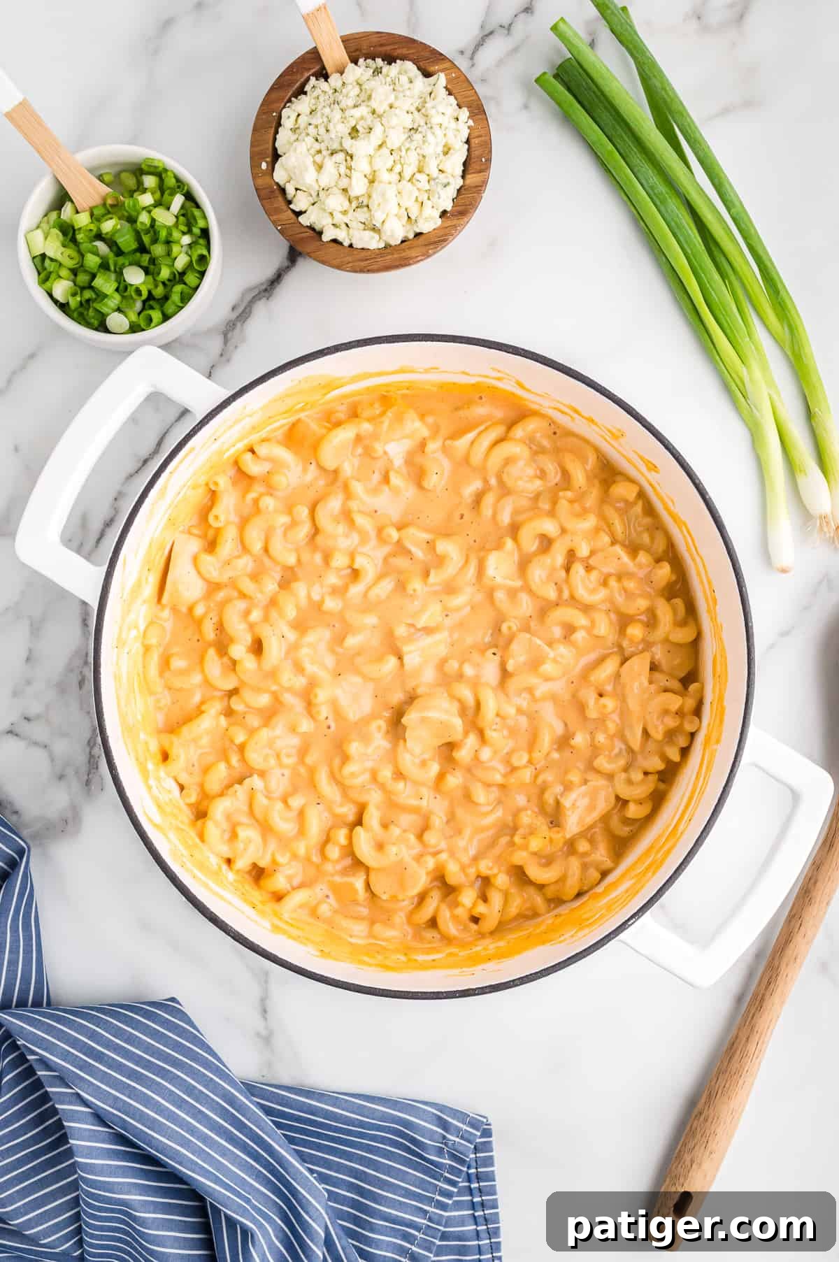 Buffalo Bliss Mac & Cheese 11 A large white pot brimming with perfectly combined Buffalo Chicken Mac and Cheese. Blue cheese crumbles and sliced green onions are arranged next to the pot, ready for garnishing.