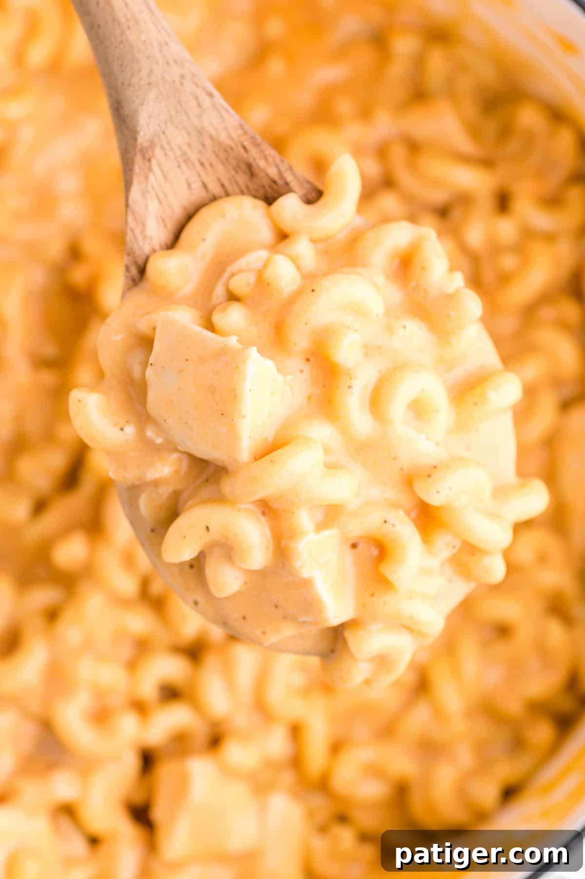 Buffalo Bliss Mac & Cheese 13 A wooden spoon scoops a creamy, cheesy portion of Buffalo Chicken Mac and Cheese with tender chicken pieces from a large white pot, highlighting its rich texture.