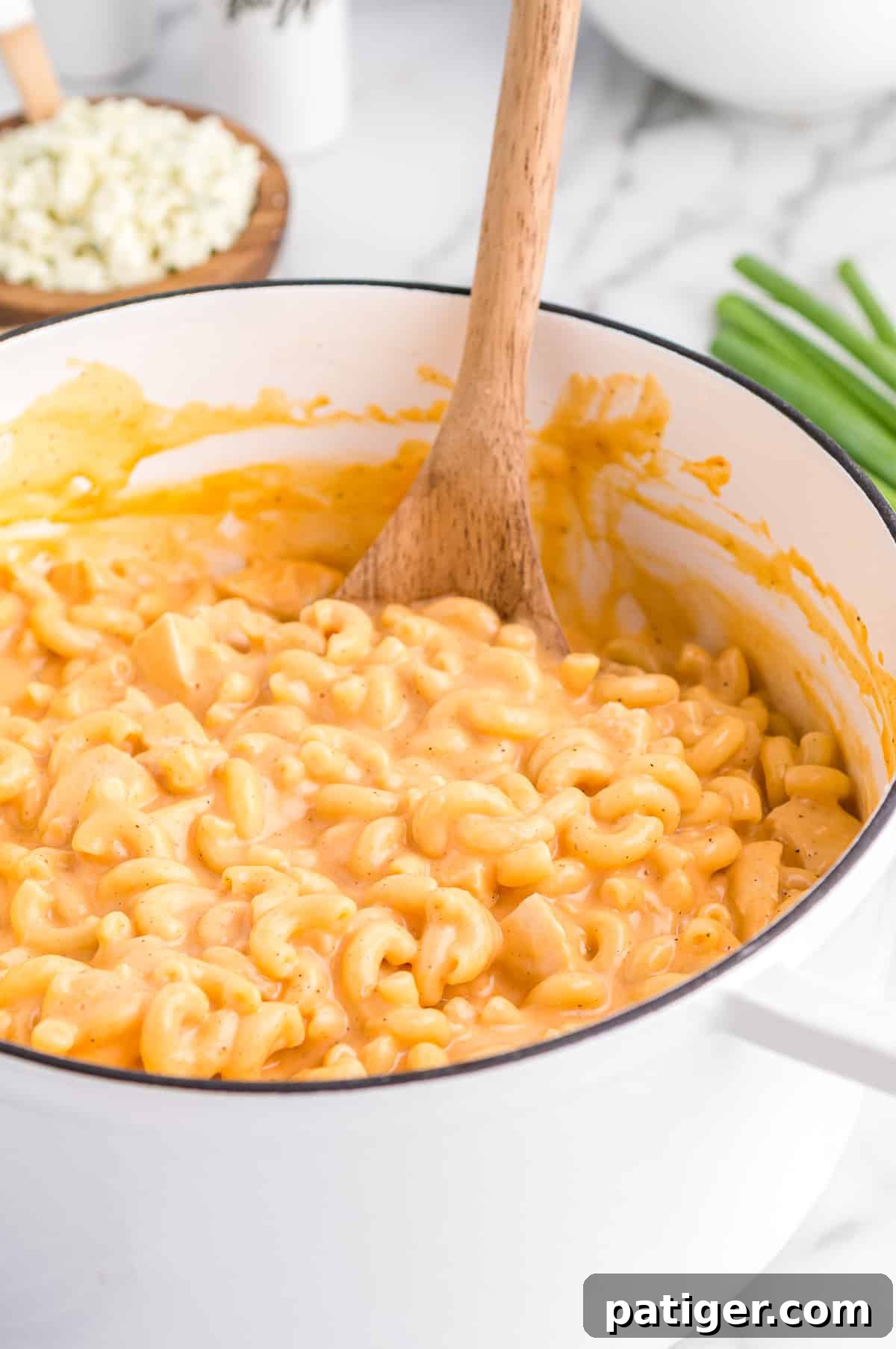 Buffalo Bliss Mac & Cheese 3 A large white pot filled with a generous portion of Buffalo Chicken Mac and Cheese, topped with sprinkles of blue cheese crumbles and fresh green onions, inviting a comforting meal.
