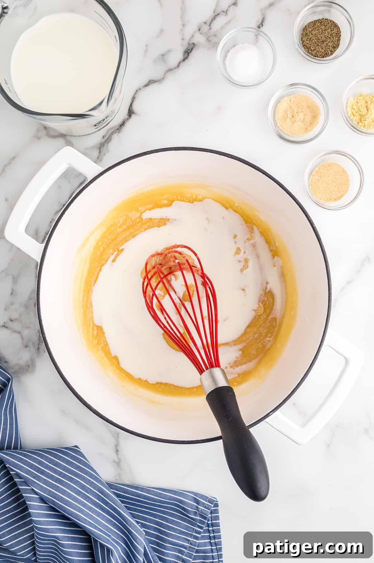 Buffalo Bliss Mac & Cheese 7 Milk being slowly whisked into the roux in a large white pot, creating a creamy white sauce base for the mac and cheese.