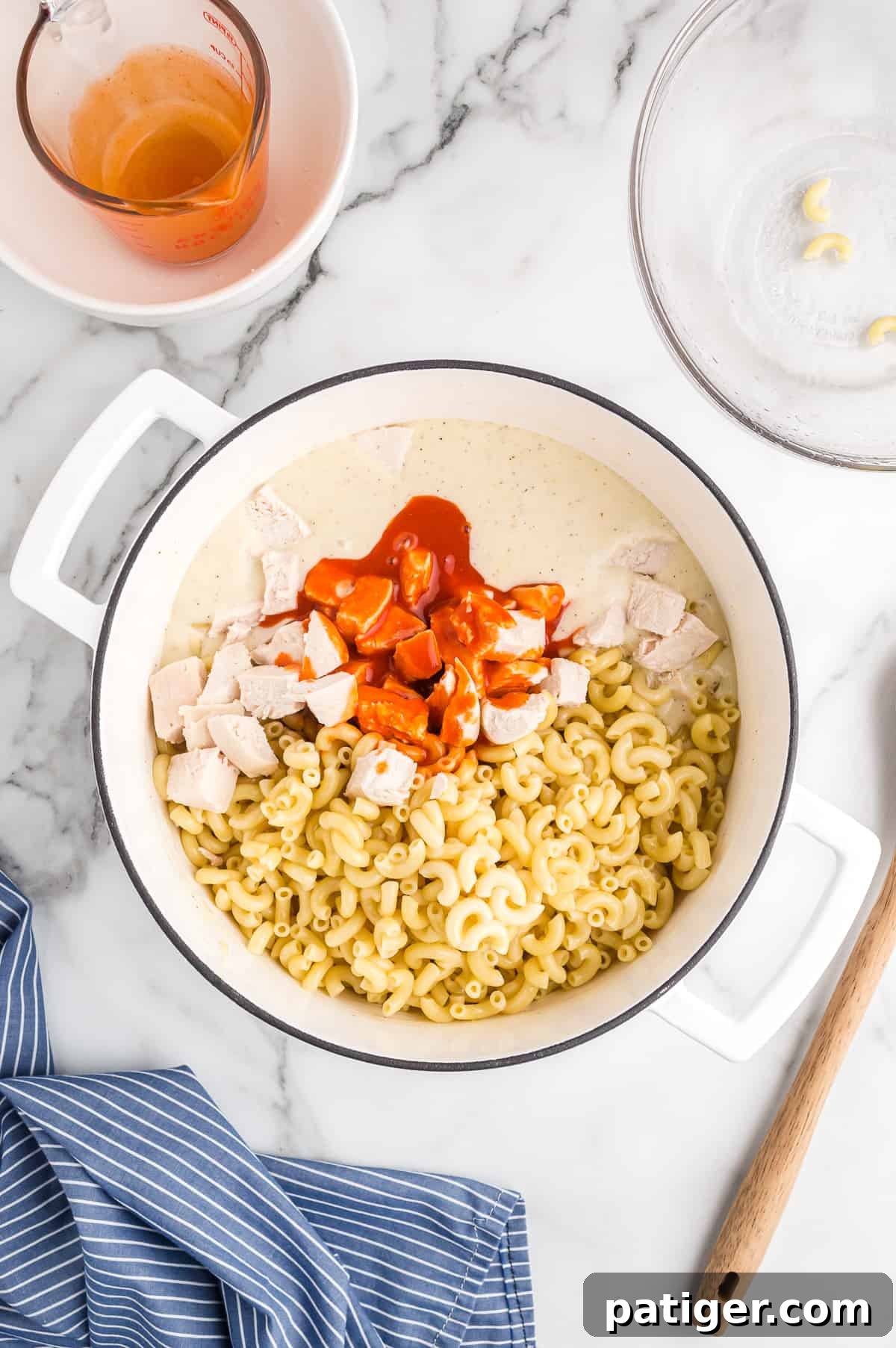 Buffalo Bliss Mac & Cheese 10 Cooked macaroni, buffalo sauce, and diced chicken being added to the large pot of rich cheese sauce, ready to be combined into a flavorful meal.