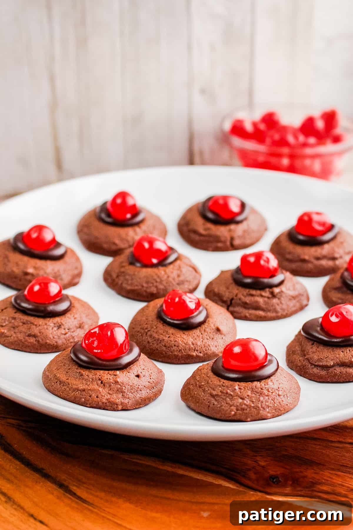 Double chocolate cherry cookies cooling on a wire rack, glistening with ganache and bright red cherries.