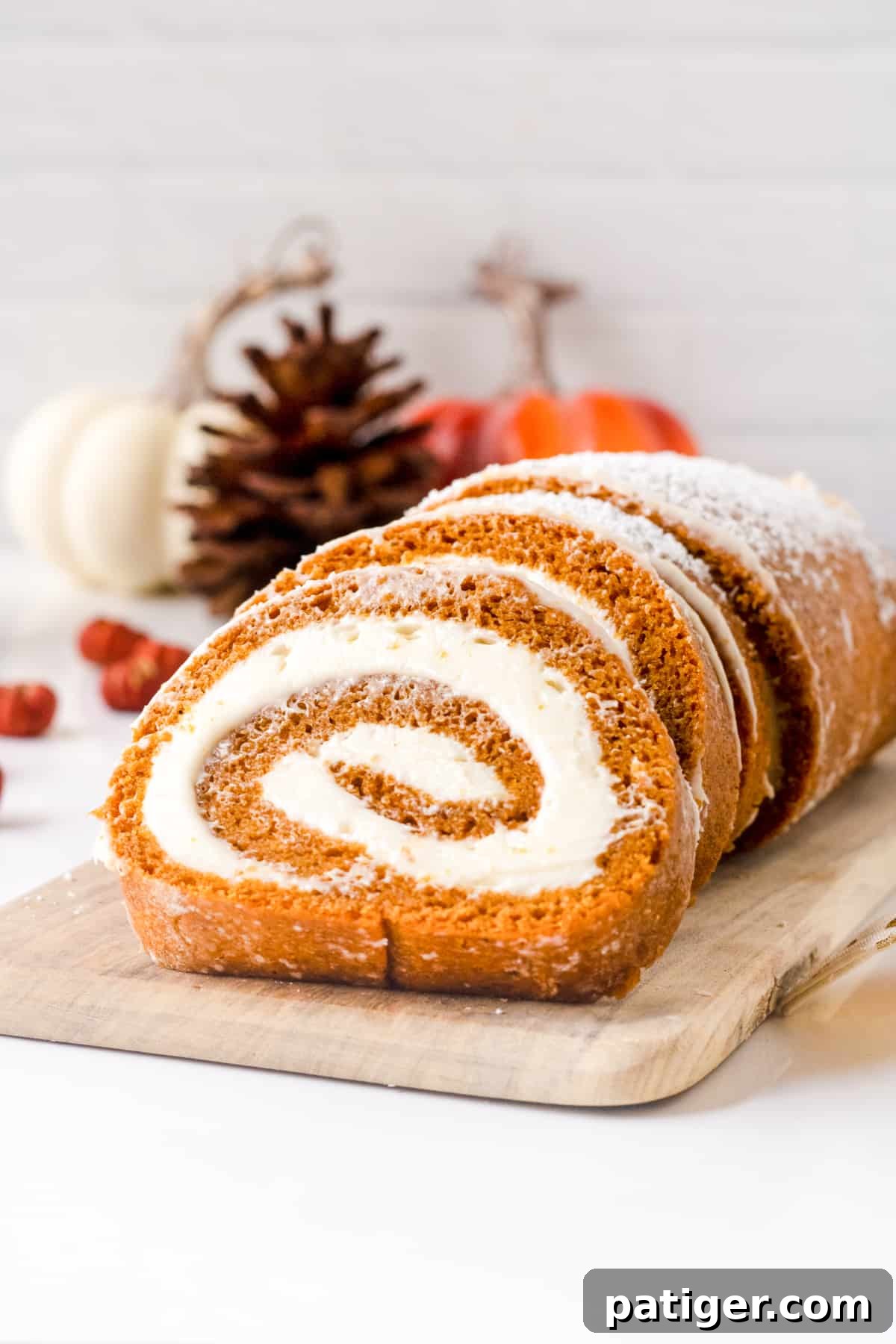 Spiced Pumpkin Swirl Cake 2 Pumpkin roll cake with cream cheese filling, dusted with powdered sugar, ready to be served on a wooden board.