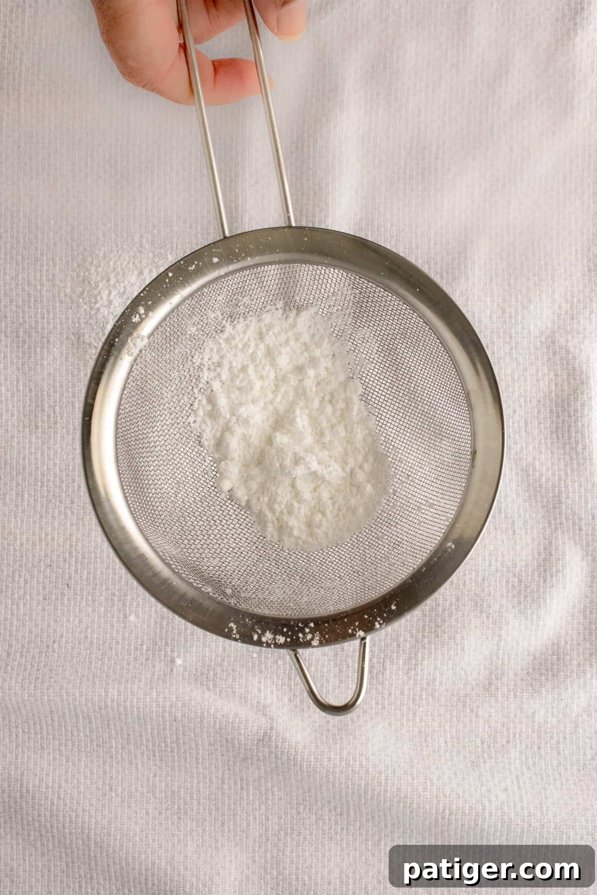 Spiced Pumpkin Swirl Cake 6 Powdered sugar being sifted onto a clean kitchen towel.