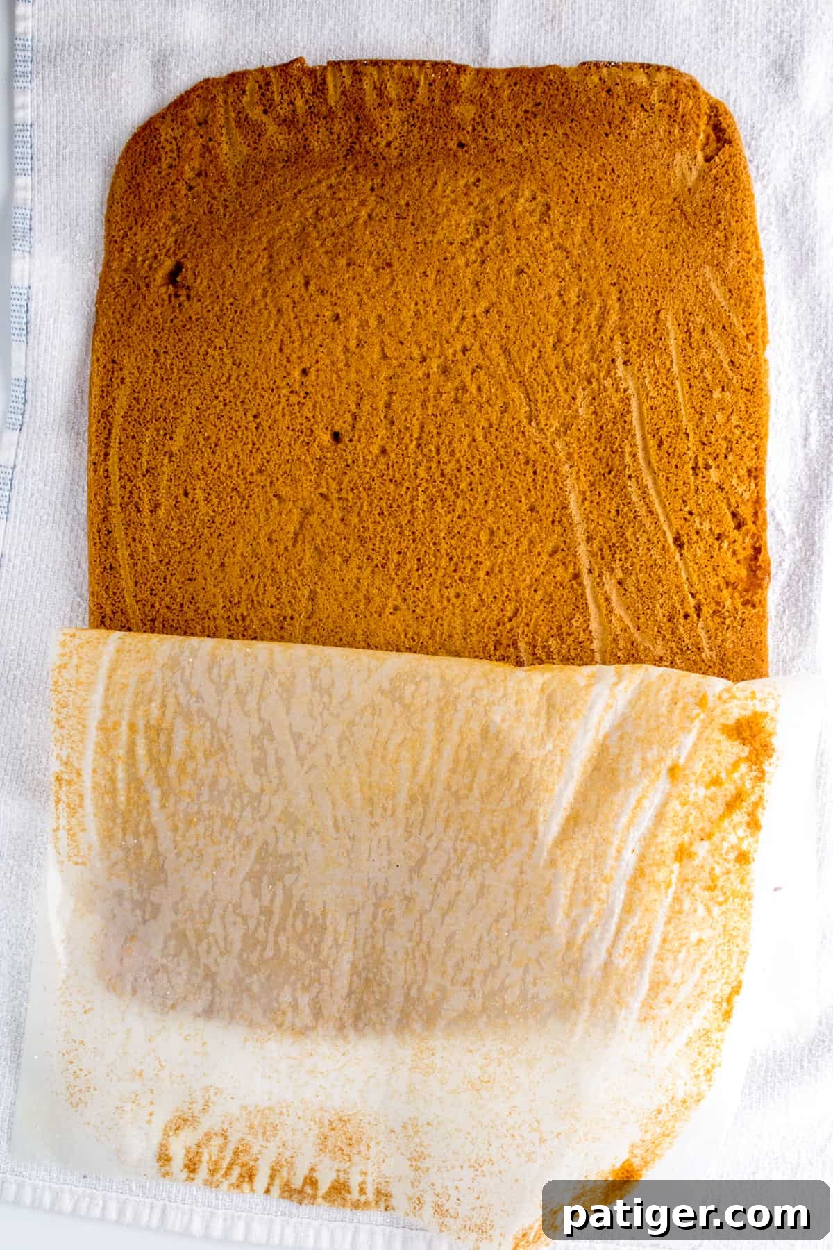 Spiced Pumpkin Swirl Cake 7 Parchment paper being carefully peeled off a warm pumpkin cake on a tea towel.