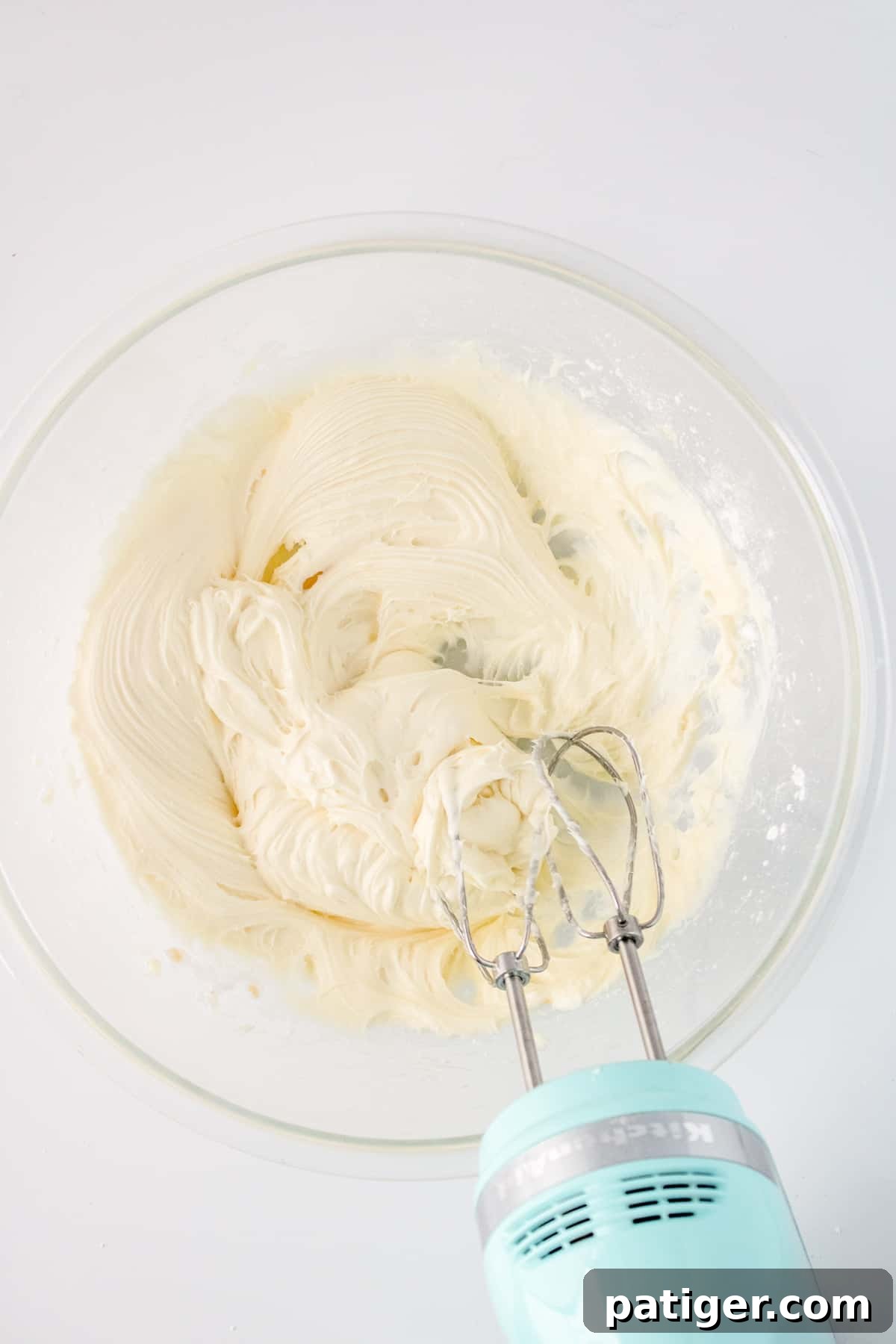 Spiced Pumpkin Swirl Cake 9 Cream cheese filling being whipped to a smooth consistency with a hand mixer in a glass bowl.