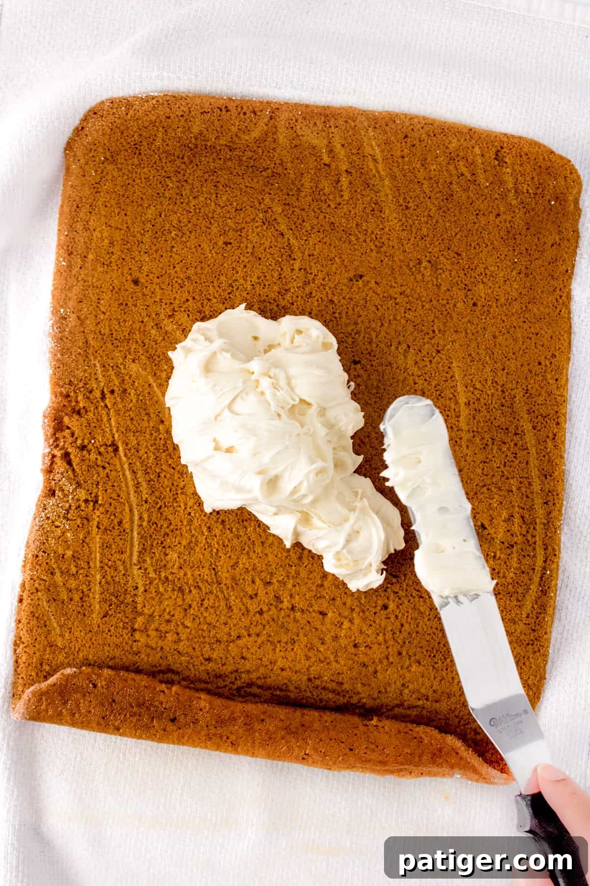 Spiced Pumpkin Swirl Cake 10 Cream cheese frosting being spread with an offset spatula onto an unrolled pumpkin cake.