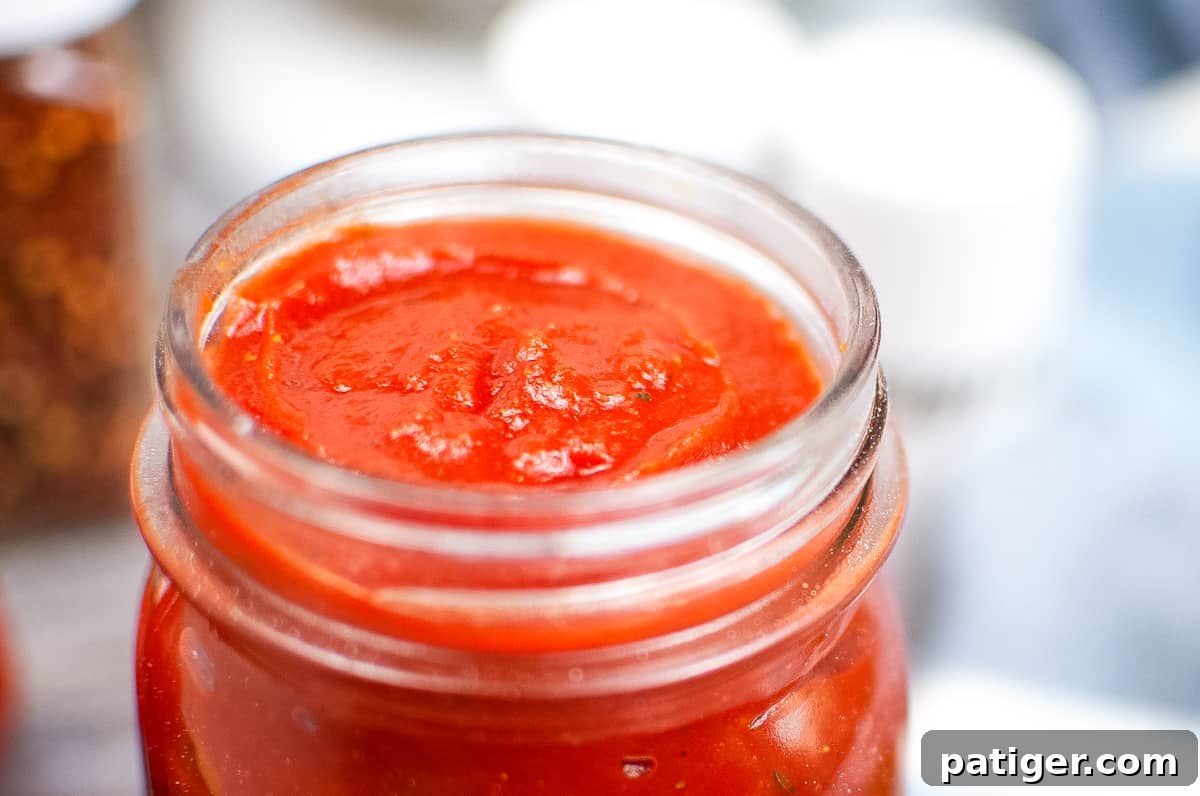 Close up photo of thick, rich homemade pizza sauce in a glass mason jar, showcasing its smooth texture.