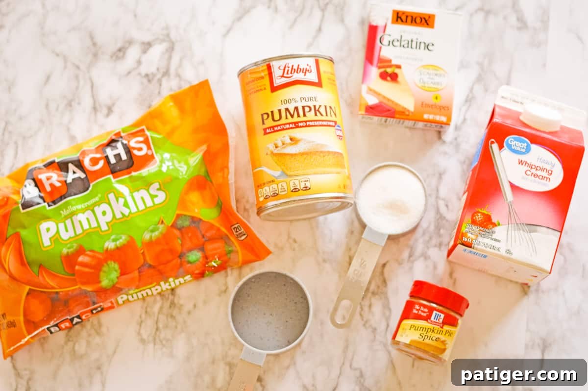 Ingredients on countertop: bag of Brach's candy pumpkins, can of Libby's 100% pumpkin, Knox unflavored gelatin, carton of heavy cream, pumpkin pie spice in a jar, measuring cup of sugar, and measuring cup of water