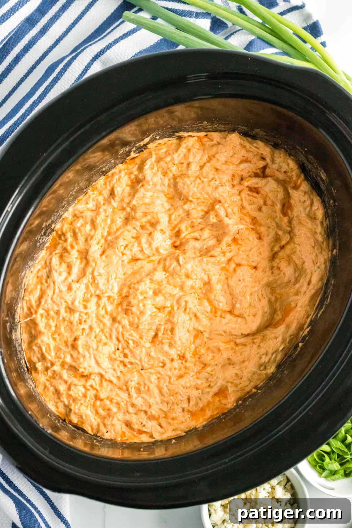 Game Day Crockpot Buffalo Chicken Dip 2 Buffalo chicken dip in the crockpot with green onions and crumbled blue cheese in the background, ready to be served.