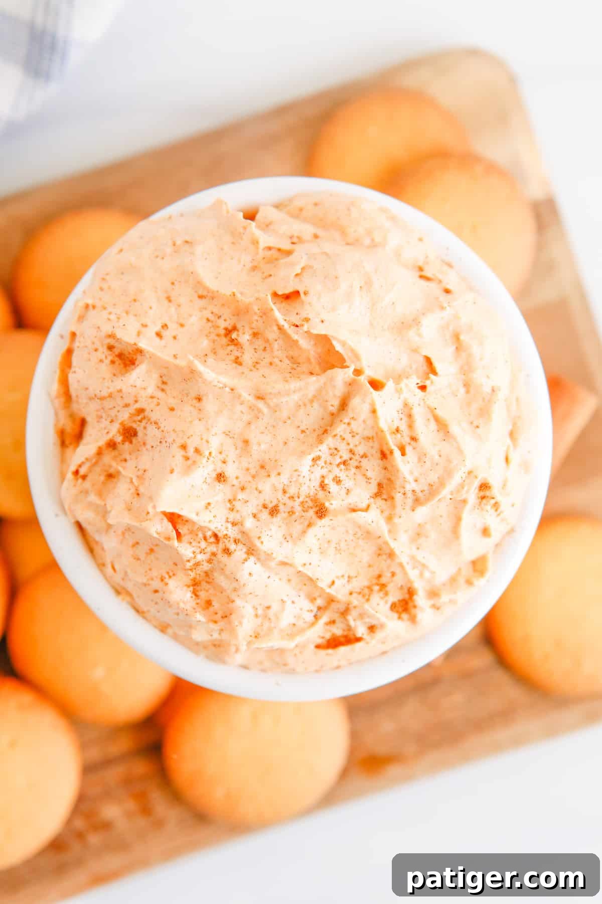 Pillowy Pumpkin Delight 3 An inviting overhead view of a pristine white bowl filled with light and airy pumpkin fluff dip, surrounded by a generous scattering of vanilla wafers, ready for sharing and enjoyment.