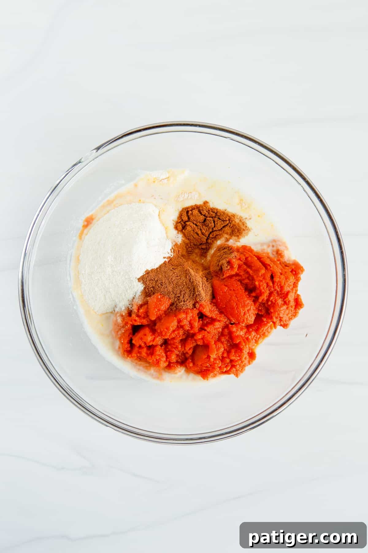 Pillowy Pumpkin Delight 6 A glass mixing bowl holds the initial ingredients for pumpkin fluff dip: milk, instant vanilla pudding mix, rich pumpkin puree, and aromatic pumpkin pie spice, all ready to be combined.