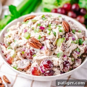 Signature Grape and Pecan Chicken Salad 7 A vibrant chicken grape and pecan salad in a white bowl, with fresh red grapes, celery, and lettuce visible in the background, suggesting a fresh and wholesome meal.