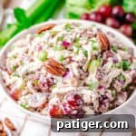 Signature Grape and Pecan Chicken Salad 8 Chicken grape and pecan salad in a white bowl, visually appealing and ready to be served, accompanied by fresh red grapes, celery, and lettuce.