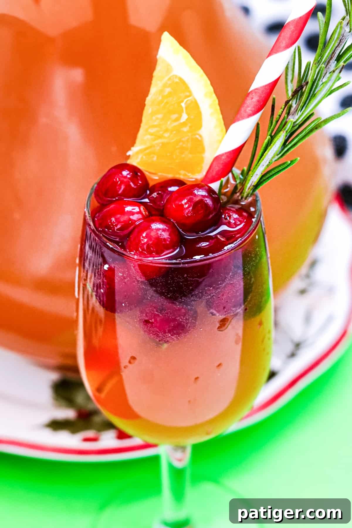 Yuletide Elixir 3 Wine glass with cranberry champagne punch topped with fresh cranberries, orange wedge, sprig of rosemary, and paper straw