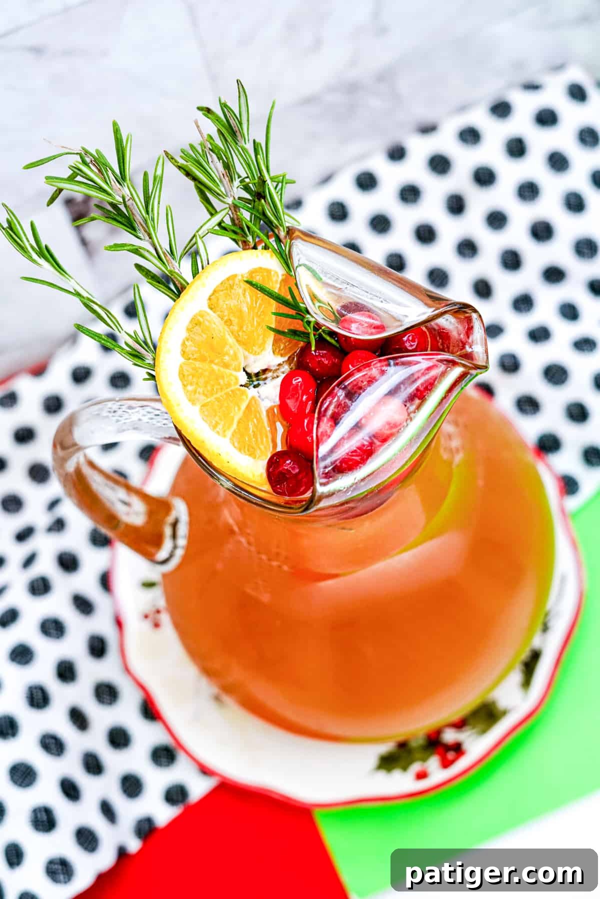Yuletide Elixir 6 Overhead view of pitcher of punch garnished with rosemary, orange slice, and cranberries