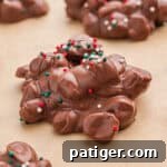 Crock pot candy (aka chocolate peanut clusters) with Christmas sprinkles on parchment paper.