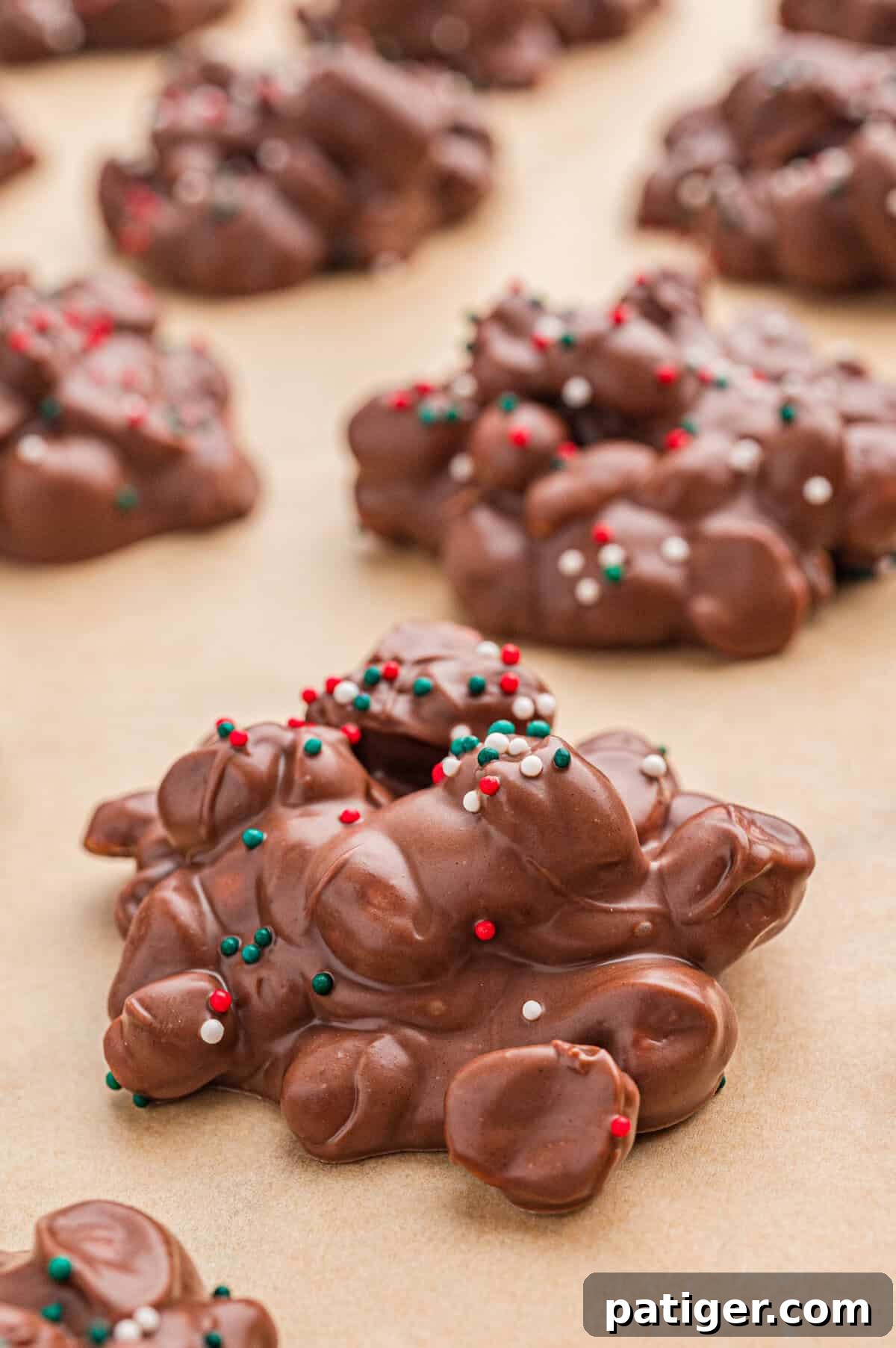 Rows of crockpot candy, chocolate peanut clusters, with Christmas sprinkles on parchment.