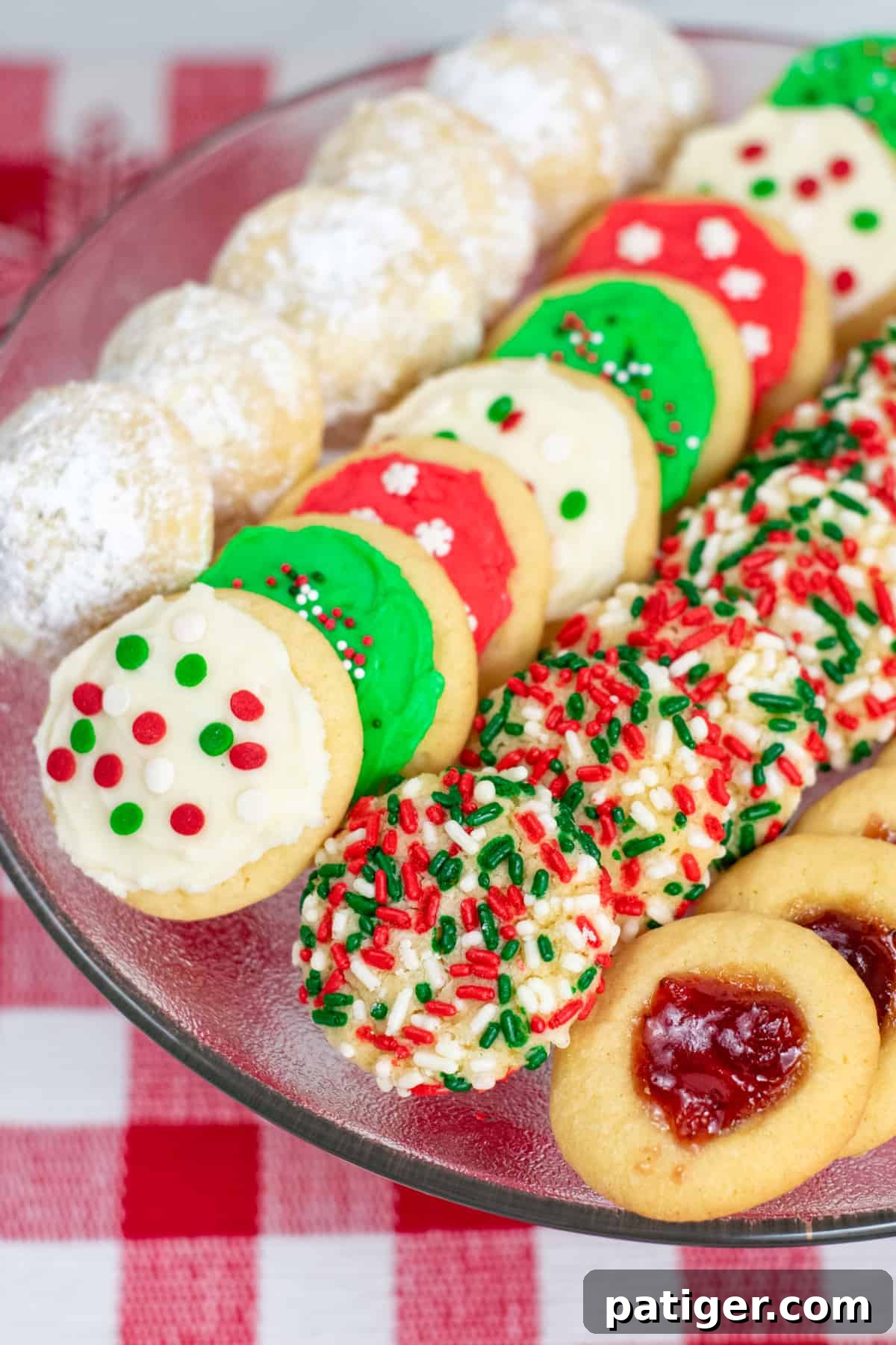 A festive holiday tray displaying four distinct types of Christmas cookies: powdered sugar-dusted cookies, elegantly frosted cookies, cheerfully sprinkled cookies, and classic jam-filled cookies.