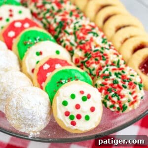 powdered sugar covered hidden kiss cookies, frosted Christmas cookies, sprinkle Christmas cookies, and thumbprint cookies with jam on a platter