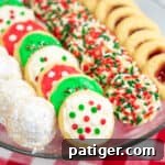 powdered sugar covered hidden kiss cookies, frosted Christmas cookies, sprinkle Christmas cookies, and thumbprint cookies with jam on a platter