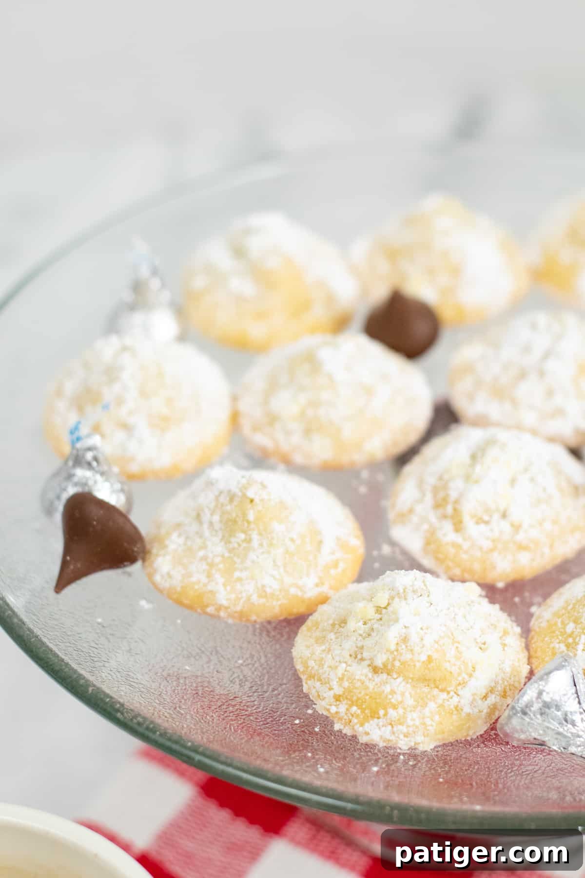 soft sugar cookies stuffed with chocolate kisses and rolled in powdered sugar. Unwrapped kisses are on platter with cookies.