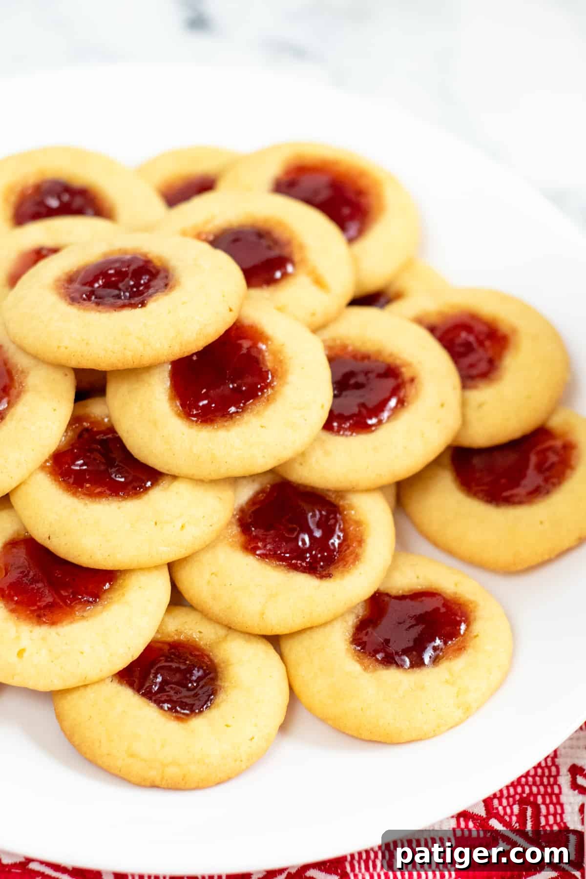 Dreamy Pudding Thumbprints 2 A festive pile of thumbprint cookies with glistening jam centers on a white plate, ready for holiday serving.