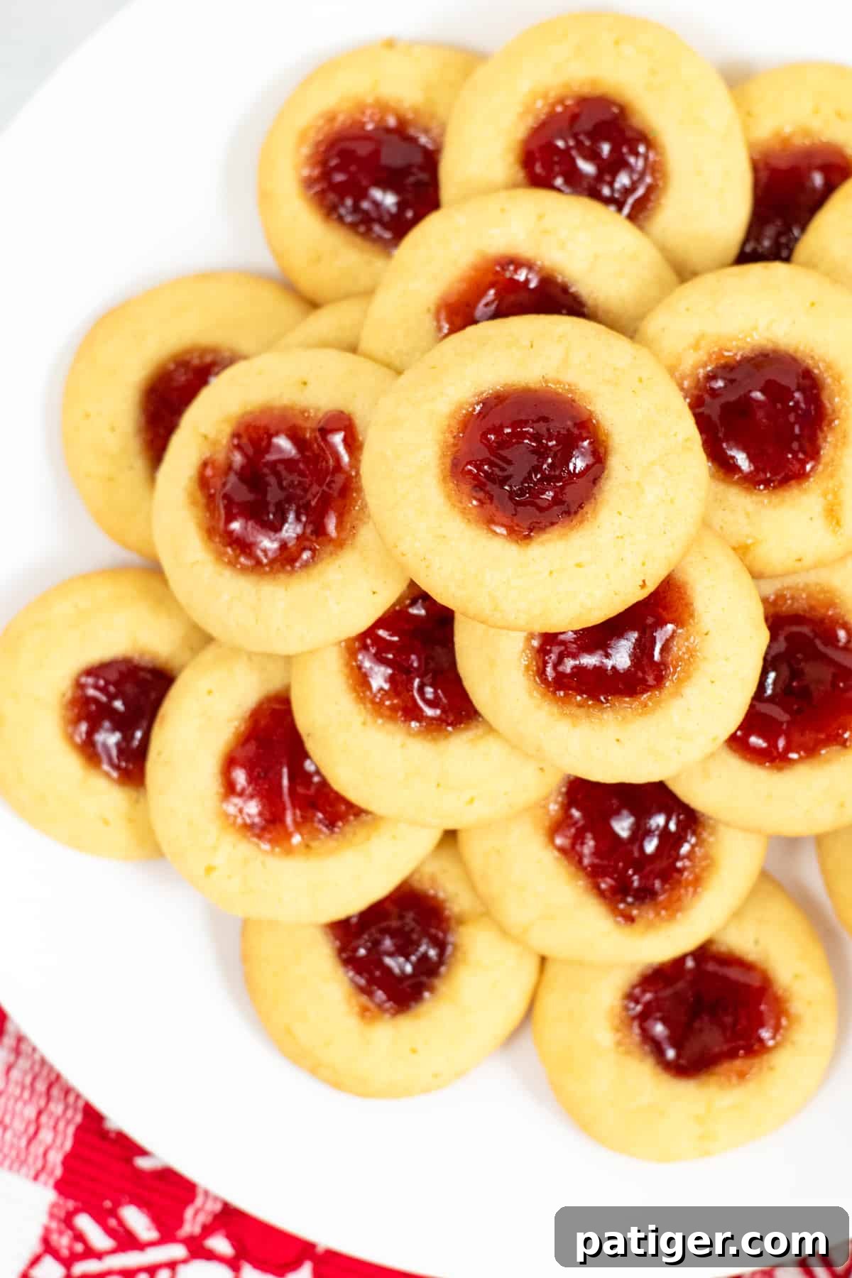 Dreamy Pudding Thumbprints 4 A top-down view of beautifully arranged strawberry jam-filled thumbprint cookies, stacked invitingly on a white plate.