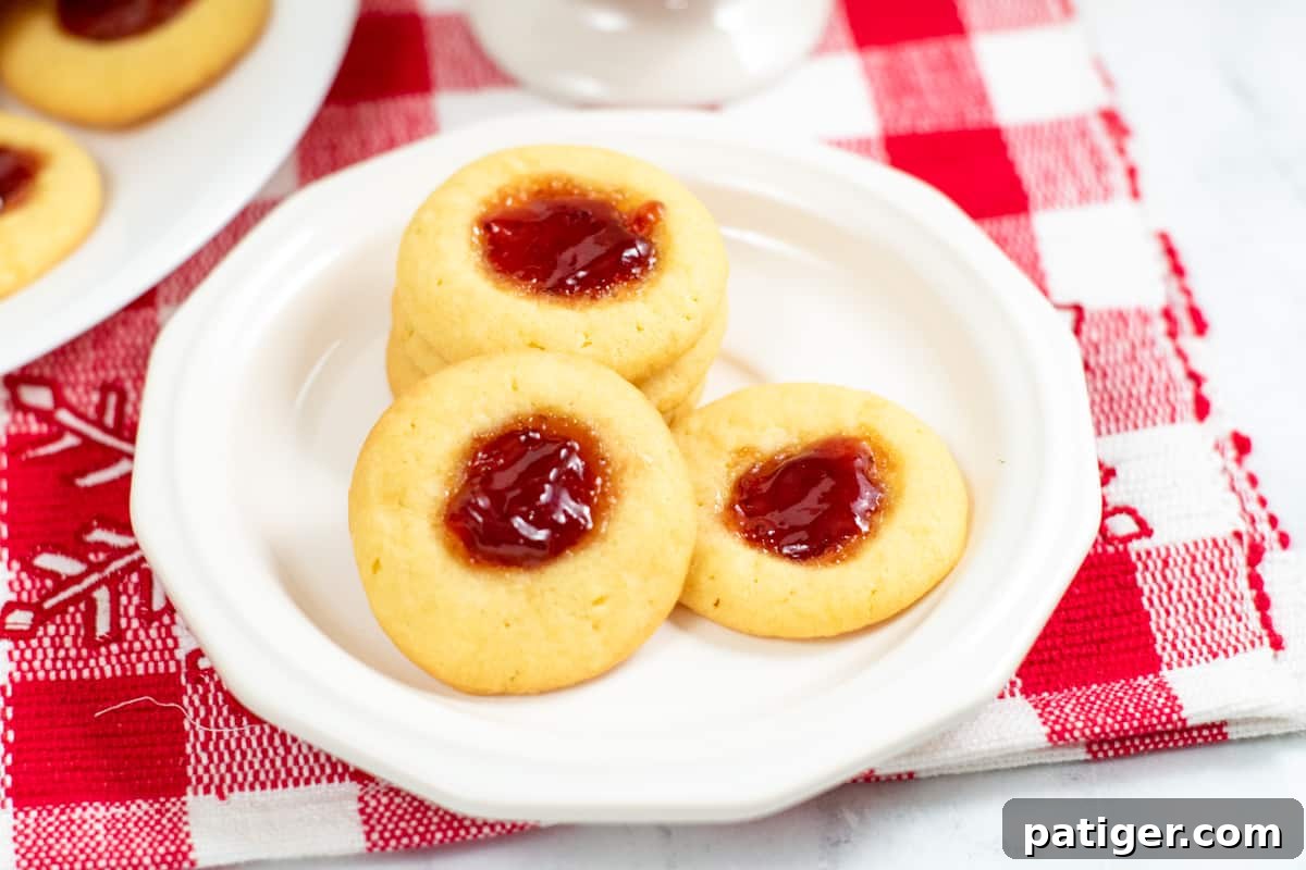 Dreamy Pudding Thumbprints 8 Freshly baked strawberry jam thumbprint cookies artfully arranged on a white plate, resting on a red and white checkered placemat.