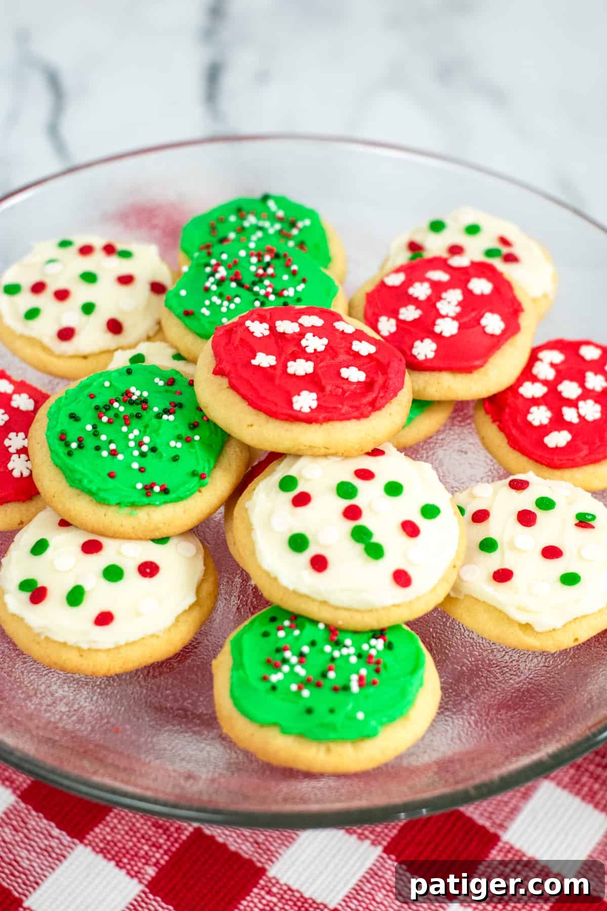 Platter of round frosted sugar cookies decorated with red, green, and white frosting and christmas sprinkles, showcasing their festive appeal.