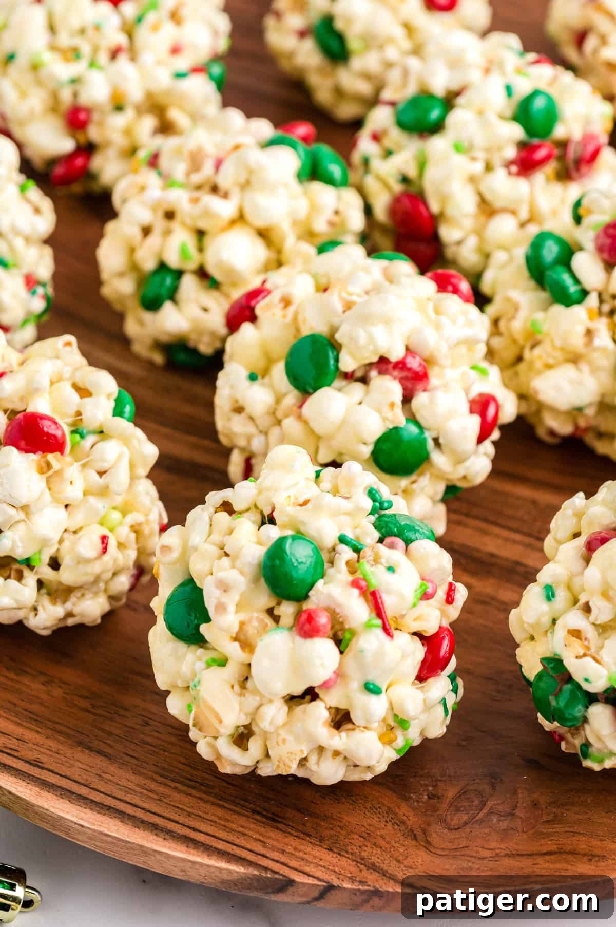 Festive Christmas popcorn balls adorned with red and green M&Ms and colorful sprinkles, arranged on a rustic wooden serving platter.