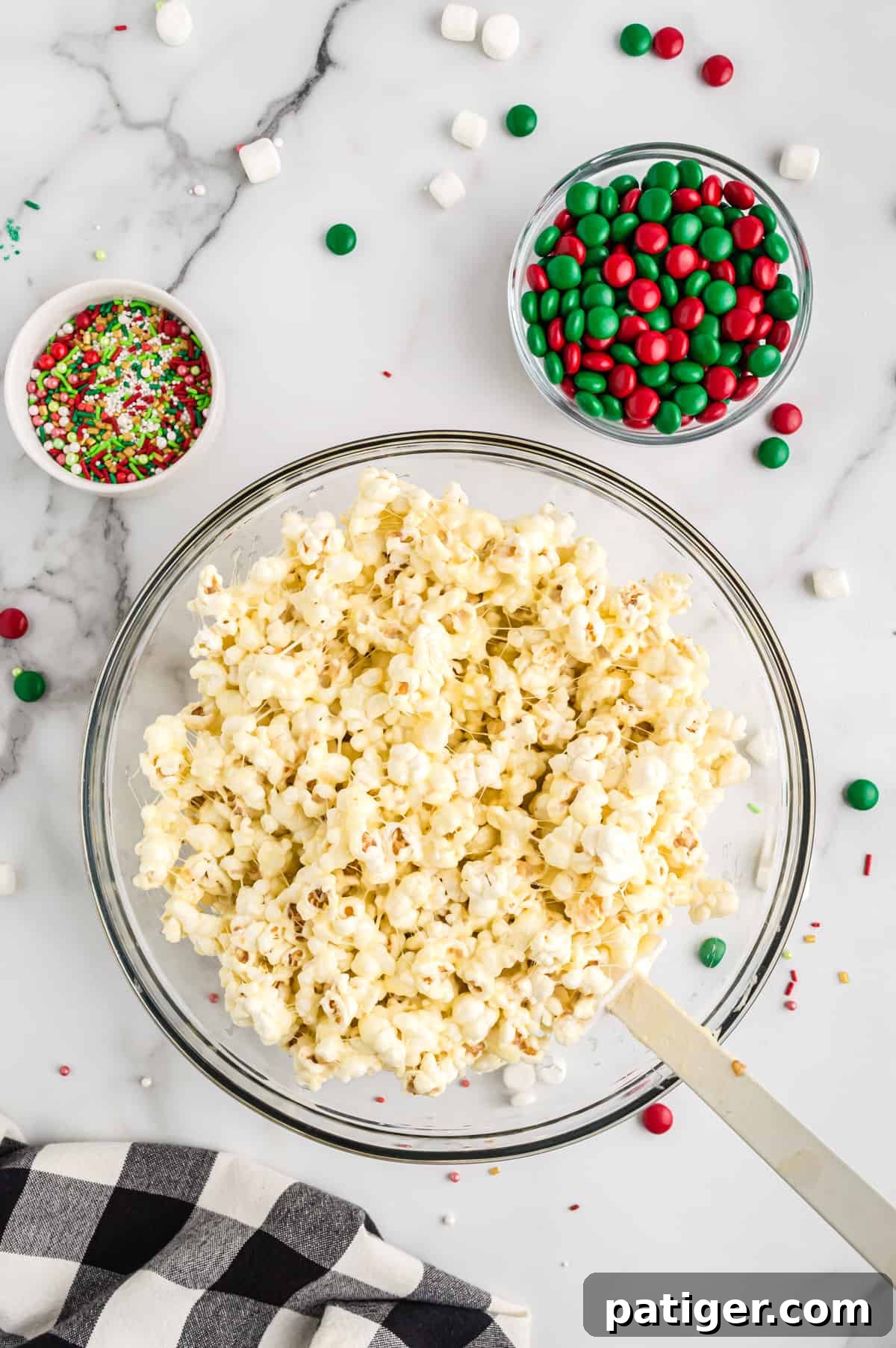 Popped popcorn being mixed with the melted butter and marshmallow mixture in a large bowl, ensuring even coating.