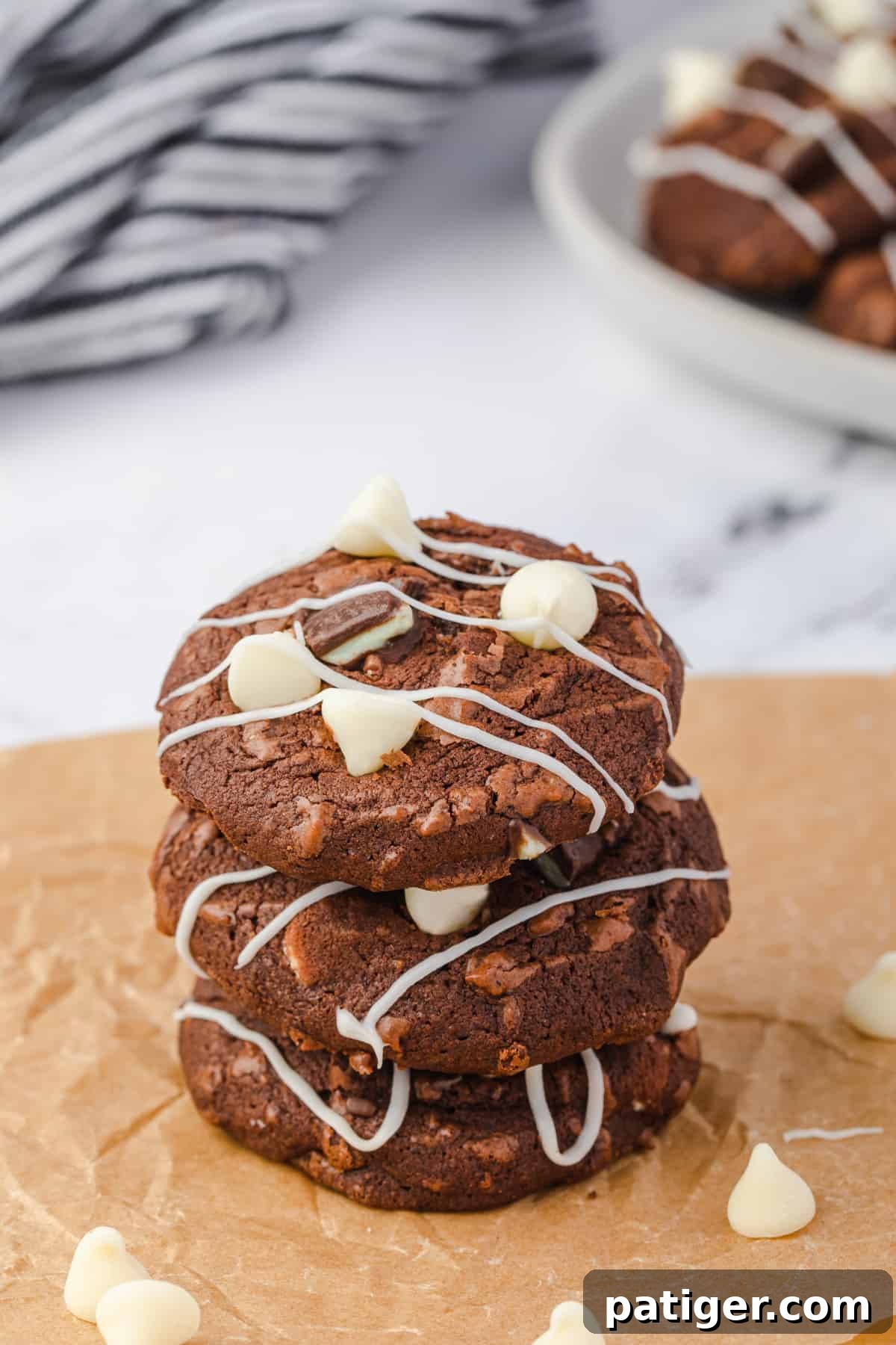 Three stacked Andes Mint Brownie Cookies with white chocolate chips, chopped Andes mints, and a beautiful white chocolate drizzle. The cookies are rich brown with green mint flecks.