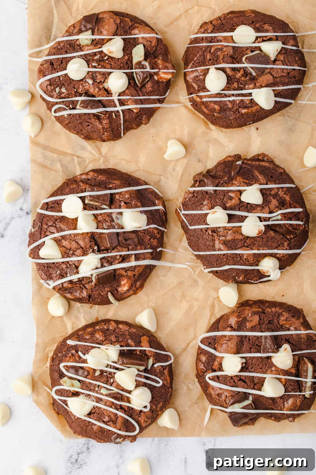 Freshly baked Andes Mint Brownie Cookies cooling on parchment paper, adorned with white chocolate chips, Andes mint pieces, and a beautiful white chocolate drizzle.