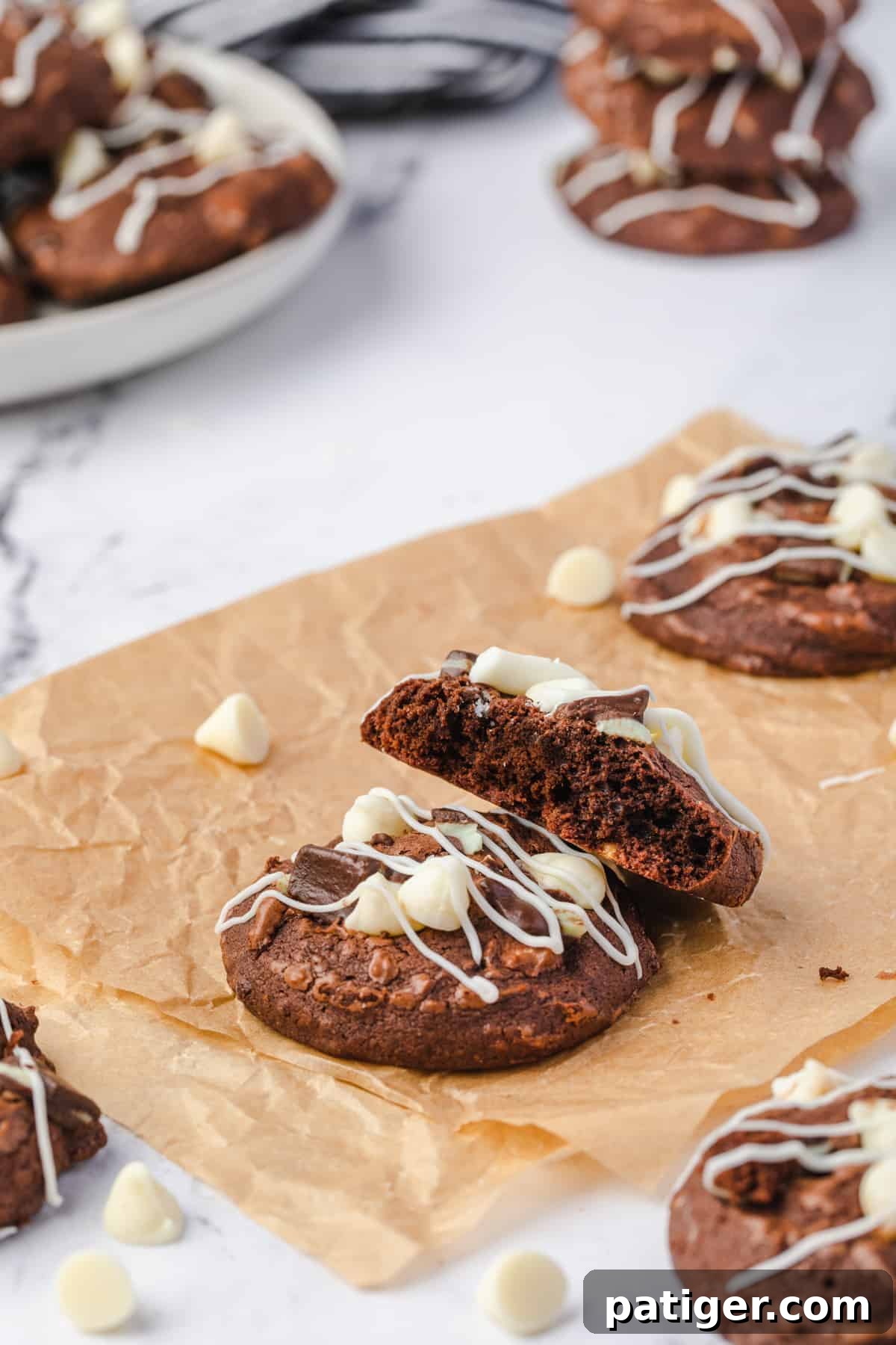 A single Andes Mint Brownie Cookie, cut in half to beautifully reveal its rich, fudgy interior and the delightful distribution of white chocolate chips and Andes mint pieces.