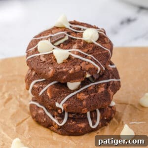 Three stacked mint chocolate brownie cookies with white chocolate chips, chunks of andes mints, and white chocolate drizzle.