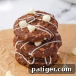 Three stacked mint chocolate brownie cookies with white chocolate chips, chunks of andes mints, and white chocolate drizzle.