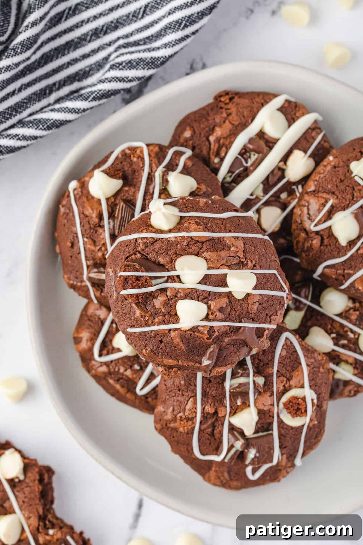 A serving plate generously piled with Andes Mint Brownie Cookies, featuring prominent white chocolate chips and elegant white chocolate drizzle.