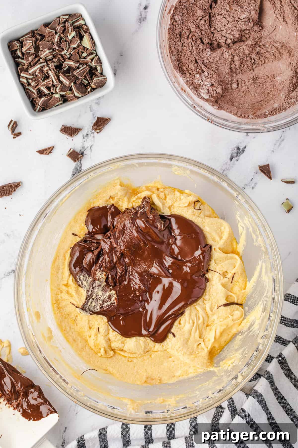 Rich melted bittersweet chocolate being poured over the creamy cookie dough ingredients in a mixing bowl, ready to be combined.