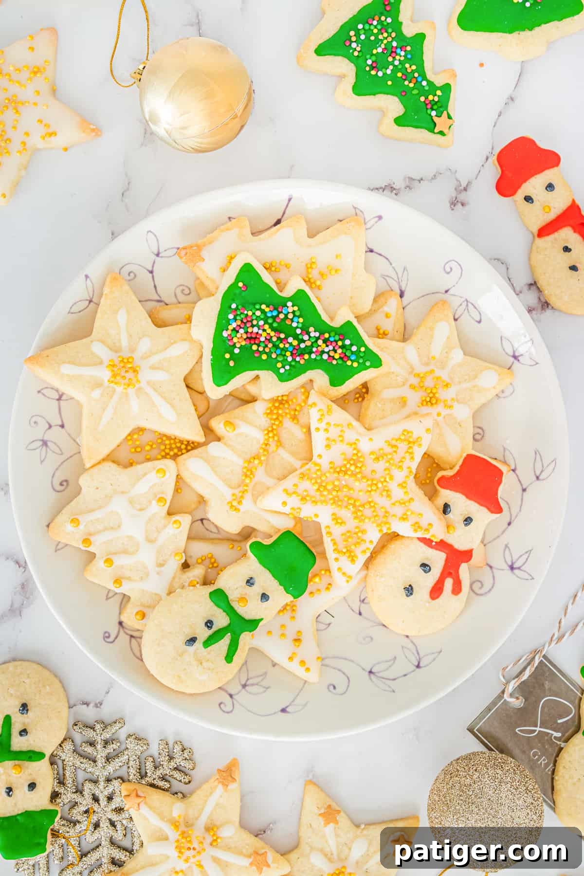 Timeless Christmas Sugar Cookie Delights 2 Decorated Christmas sugar cookies with icing and sprinkles on serving plate with additional cookies and Christmas ball ornaments scattered around table