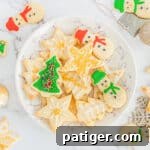 Decorated Christmas sugar cookies with icing and sprinkles on serving plate with additional cookies scattered around table