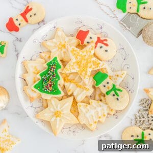 Decorated Christmas sugar cookies with icing and sprinkles on serving plate with additional cookies scattered around table