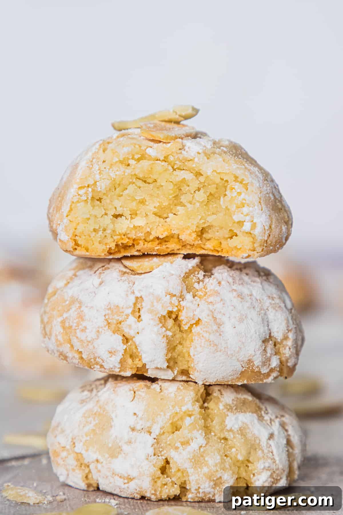 Three Italian Amaretti cookies on top of one another, with a top cookie broken in half to show soft, crumbly texture