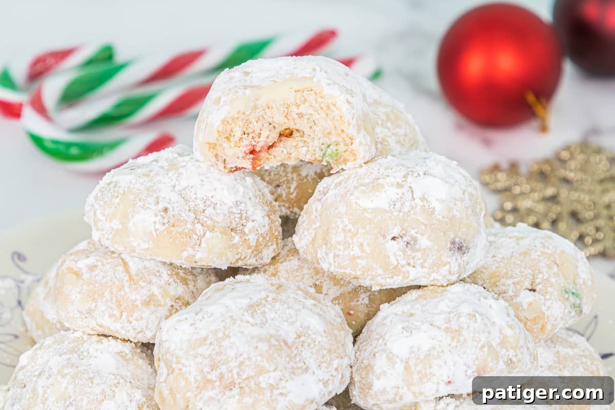 Crimson Swirl Snowball Delights 3 A stack of Peppermint Candy Cane Snowball Cookies, with the top cookie broken in half to clearly show embedded pieces of red and green crushed candy canes.