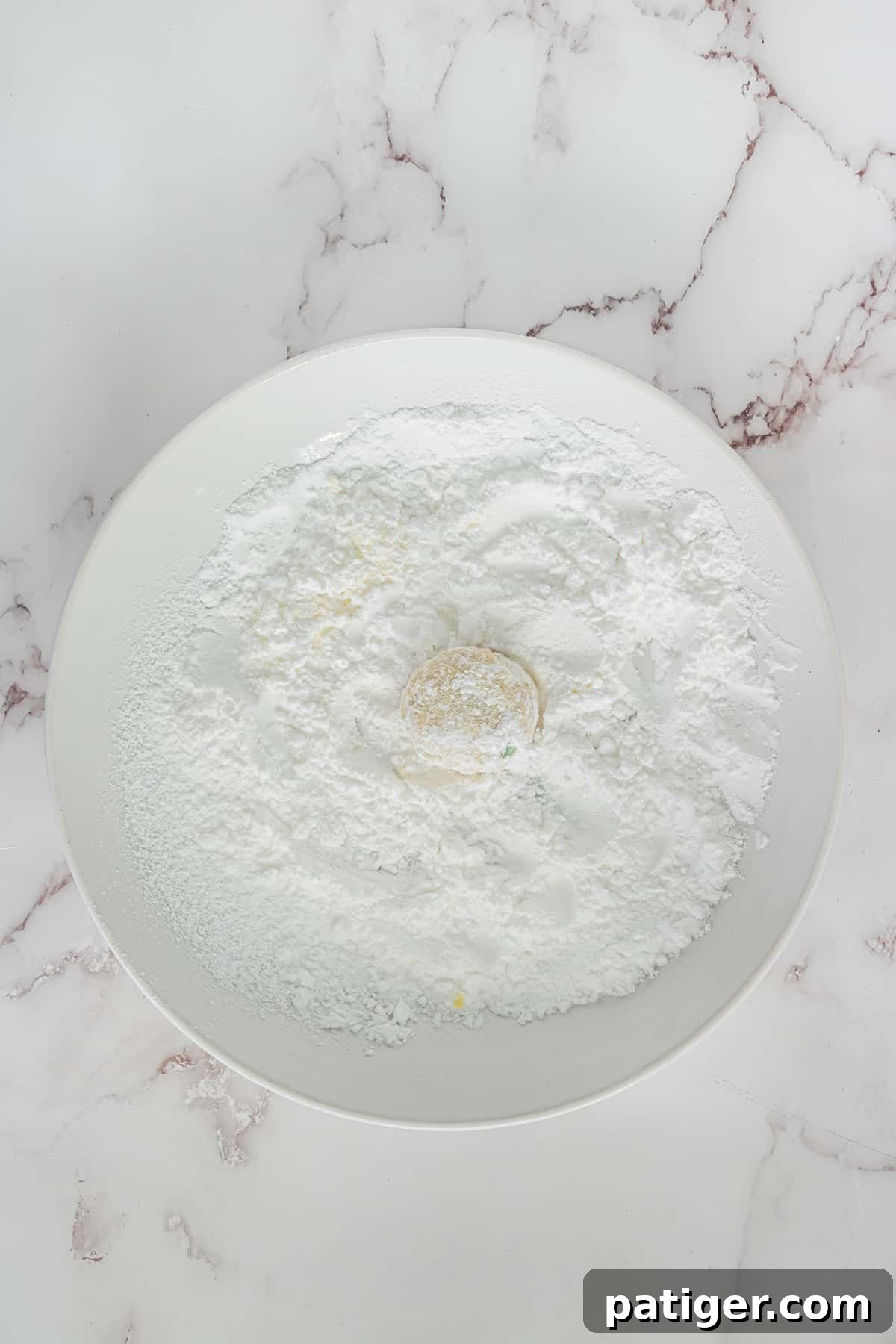 Crimson Swirl Snowball Delights 7 A close-up shot of a snowball cookie being rolled in a bowl of confectioners sugar, showcasing the creation of its signature snowy exterior.